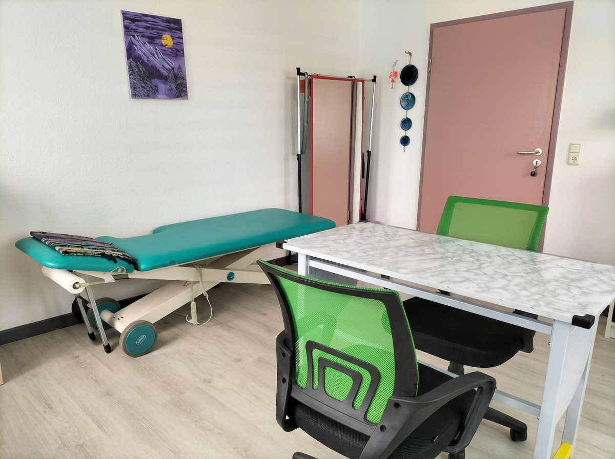 Behandlungsraum der Ergotherapiepraxis mit Therapieliege, Arbeitstisch und grünem Stuhl bei Tageslicht
