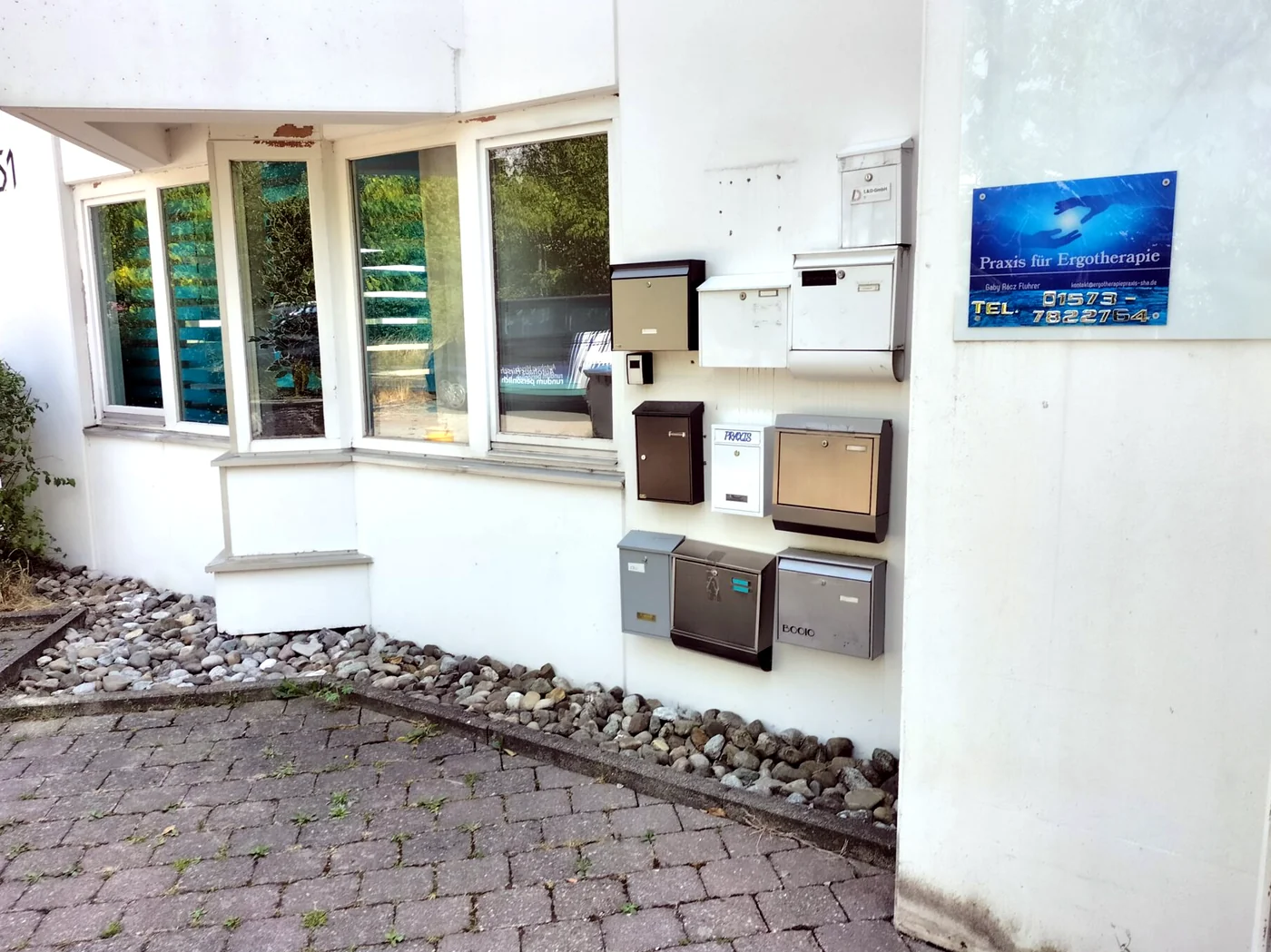 Hauseingang der Robert-Bosch-Straße 51 von außen mit Hausnummer, Briefkästen und blauem Praxisschild an der Wand